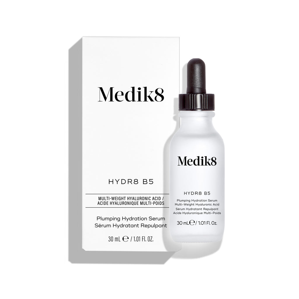 La botella del sérum Medik8 Hydr8 B5 se encuentra frente a su caja de producto blanca a juego sobre un fondo blanco limpio. El texto en ambos identifica el producto como un “Sérum líquido rehidratante” de 30 mL.
