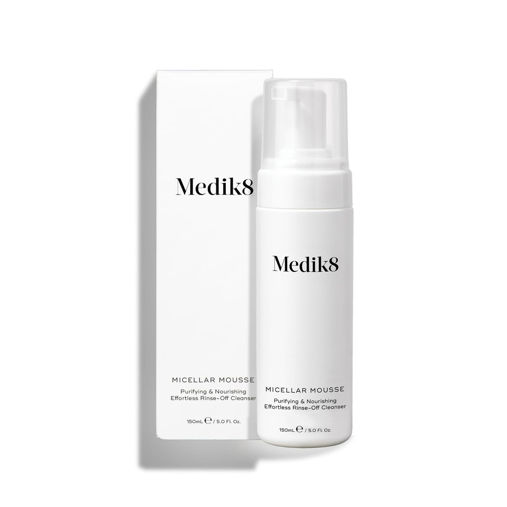 Botella con dispensador de Medik8 Micellar Mousse junto a su caja blanca de empaque sobre un fondo blanco. El texto identifica el producto como un limpiador purificante y nutritivo de fácil enjuague.