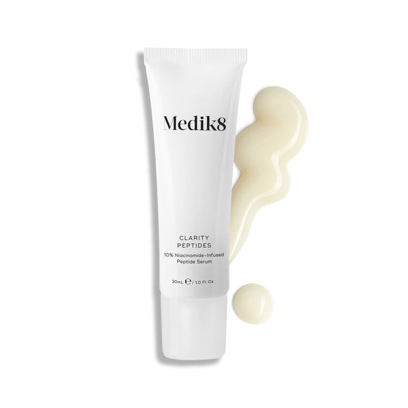 El tubo de Medik8 Clarity Peptides yace sobre un fondo blanco junto a una extensión de sérum blanco lechoso. El texto destaca la fórmula de “Sérum de Péptidos con 10 % de Niacinamida”.-19