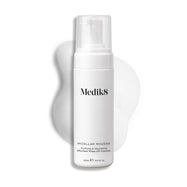 Botella con dispensador de Medik8 Micellar Mousse exhibida sobre un fondo blanco con una extensión de espuma blanca detrás, resaltando la textura del producto.