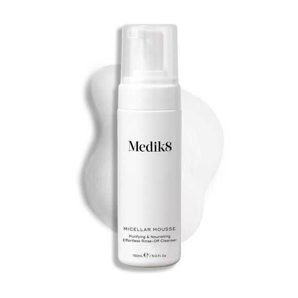 Botella con dispensador de Medik8 Micellar Mousse exhibida sobre un fondo blanco con una extensión de espuma blanca detrás, resaltando la textura del producto.-29