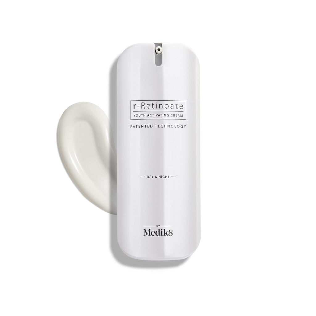 Un elegante frasco blanco con dispensador de r-Retinoate Day & Night se mantiene en posición vertical, con un remolino de crema blanca al lado.