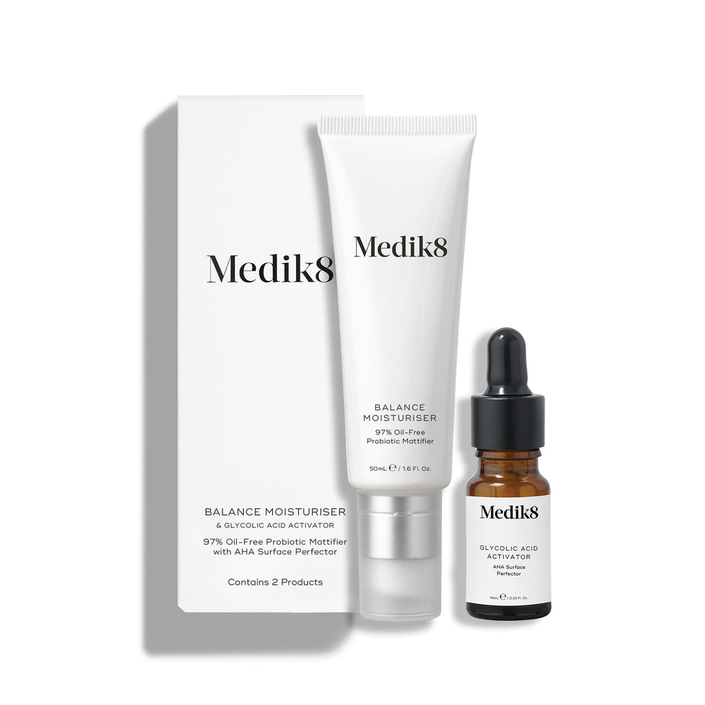 Una caja de cartón blanca se encuentra junto a un tubo blanco de Balance Moisturiser y un pequeño frasco de vidrio marrón de Glycolic Acid Activator.