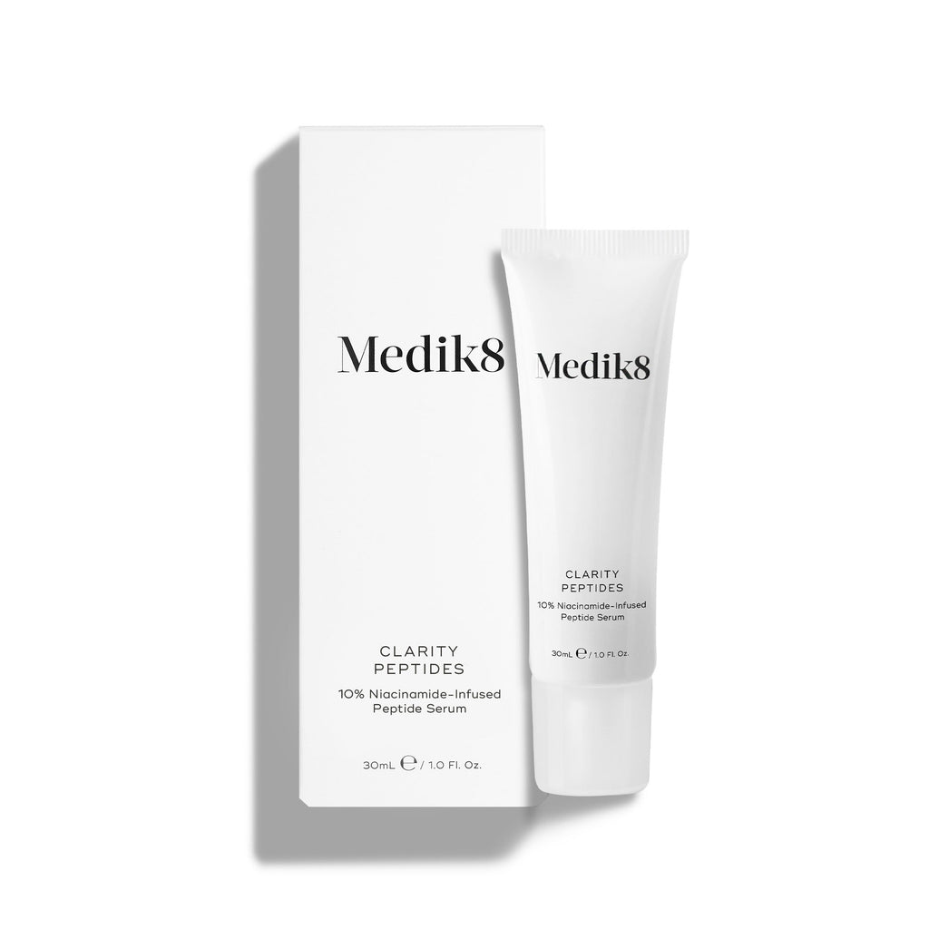 El tubo de Medik8 Clarity Peptides se encuentra junto a su caja blanca de empaque sobre un fondo blanco. El texto identifica el producto como un “Sérum de Péptidos con 10 % de Niacinamida” en un tamaño de 30 mL.