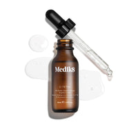 Packshot cenital de una botella de 30 mL de Medik8 C-Tetra Lipid Vitamin C Radiance Serum. La botella de vidrio ámbar está destapada y colocada en el centro, con su tapa negra con gotero apoyada diagonalmente detrás de ella. Un sérum líquido transparente está salpicado y extendido artísticamente sobre el fondo blanco limpio alrededor de la botella, con algunas gotas visibles en la pipeta de vidrio. La iluminación es brillante, proyectando sombras suaves hacia la izquierda y creando una estética clínica y el