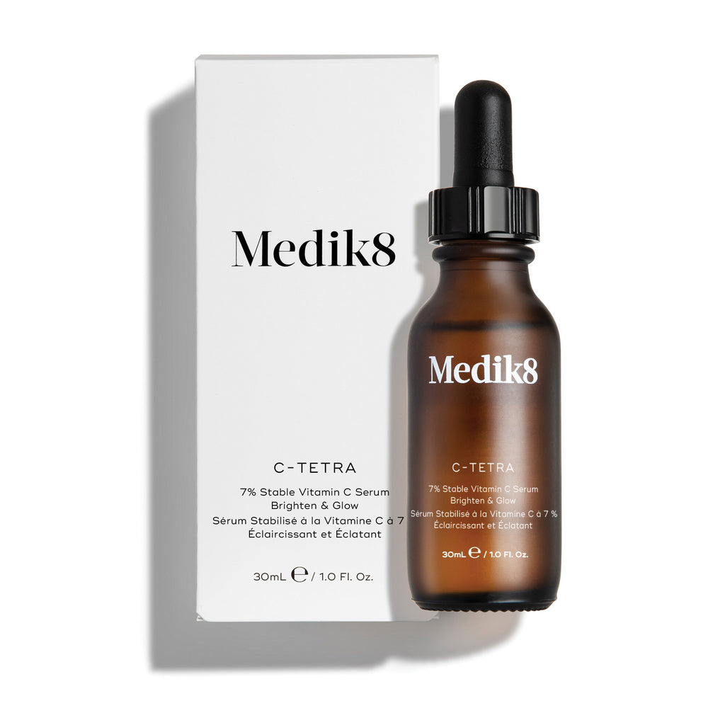 Botella del sérum Medik8 C-Tetra Luxe y su caja de cartón blanca exhibidas sobre un fondo blanco limpio con sombras suaves. La botella de vidrio ámbar y la caja blanca muestran el logotipo de Medik8 e identifican el producto como “C-TETRA LUXE Lipid Vitamin C Enhanced Radiance Serum” en un tamaño de 30 mL.