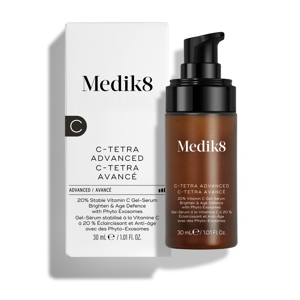 Botella ámbar con dispensador de 30 ml de Medik8 C-Tetra Advanced colocada junto a su caja de cartón blanca sobre un fondo blanco limpio. El texto de la botella y la caja dice: «Gel-sérum con 20 % de vitamina C», «Luminosidad y defensa antiedad» y «con fitoexosomas».