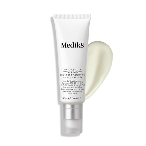 Crema hidratante Medik8 Advanced Day Total Protect SPF 30, presentada en un tubo blando blanco con tapón transparente, junto a una muestra de crema suave de color amarillo pálido sobre un fondo blanco.-21