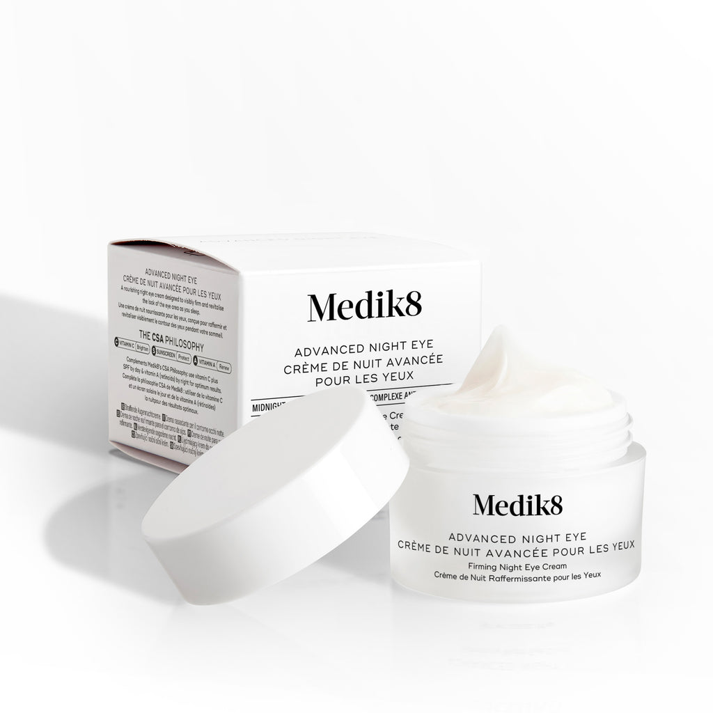 El tarro de Medik8 Advanced Night Eye aparece abierto junto a su caja de empaque sobre un fondo blanco. El texto destaca la fórmula de “Crema Rejuvenecedora para el Contorno de Ojos” y su tamaño de 15 mL.
