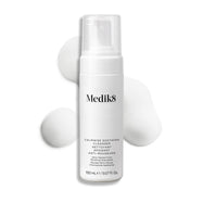 Botella con dispensador de Medik8 Calmwise Soothing Cleanser mostrada sobre un fondo blanco con una capa de espuma blanca detrás, destacando la textura del producto.