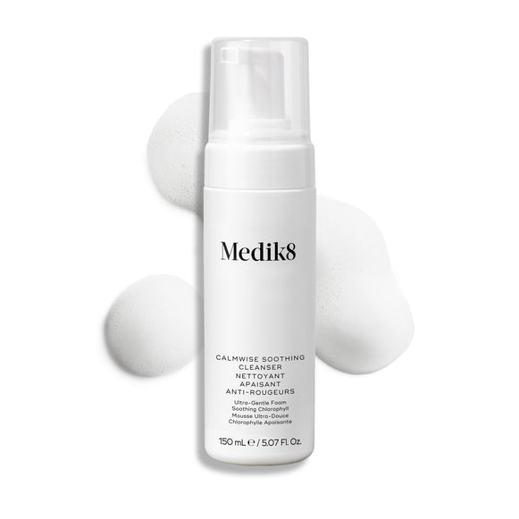 Botella con dispensador de Medik8 Calmwise Soothing Cleanser mostrada sobre un fondo blanco con una capa de espuma blanca detrás, destacando la textura del producto.-36