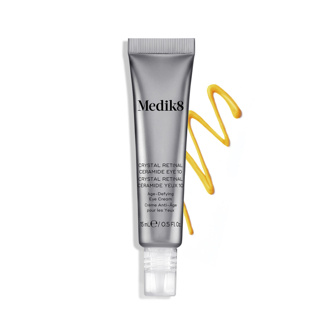 Medik8 Crystal Retinal Ceramide Eye 10: Tubo de crema junto a una muestra en zigzag de crema amarilla sobre un fondo blanco. Dos distintivos plateados destacan «GANADOR DE MÁS DE 4 PREMIOS GLOBALES» y «TECNOLOGÍA PATENTADA PRIMERA EN EL MUNDO».