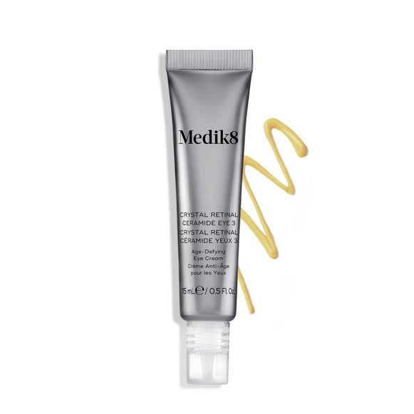Medik8 Crystal Retinal Ceramide Eye 3: Tubo de crema junto a una muestra en zigzag de crema amarilla sobre un fondo blanco. Dos distintivos plateados destacan «GANADOR DE MÁS DE 4 PREMIOS GLOBALES» y «TECNOLOGÍA PATENTADA PRIMERA EN EL MUNDO».-10