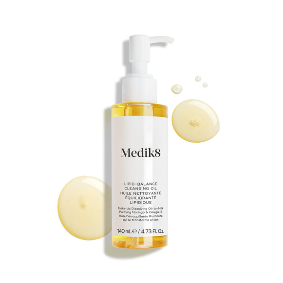 La botella de Medik8 Lipid-Balance Cleansing Oil se encuentra sobre un fondo blanco. Gotas de aceite dorado rodean la botella, resaltando su textura rica y fluida.-20