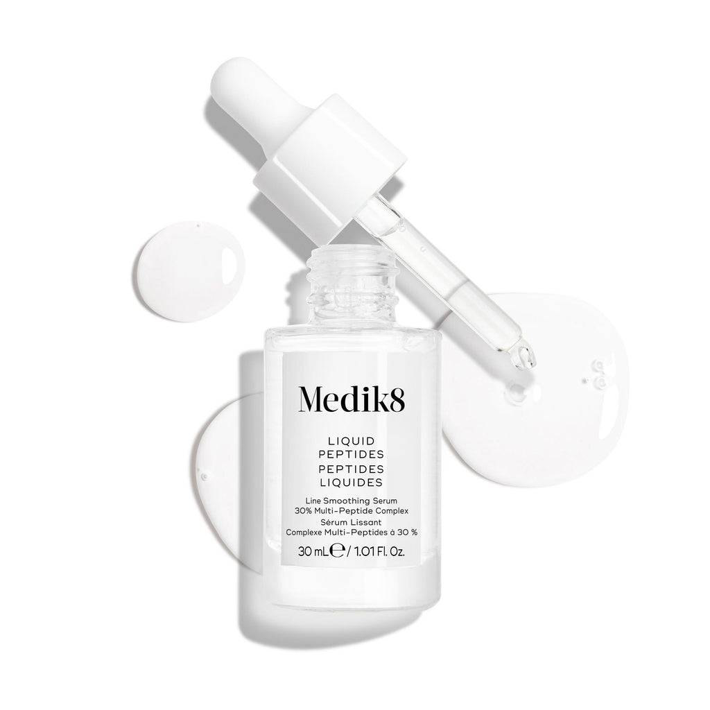 Un frasco cuentagotas de vidrio transparente del sérum Liquid Peptides se presenta con el cuentagotas retirado y colocado al lado, junto a gotas de sérum que muestran la textura del producto.