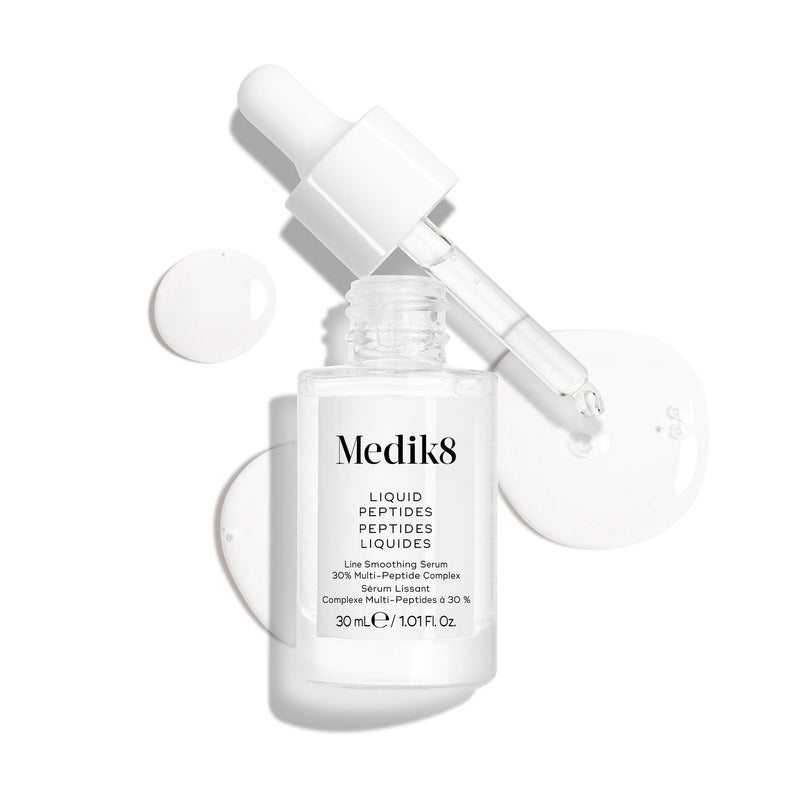 Un frasco cuentagotas de vidrio transparente del sérum Liquid Peptides se presenta con el cuentagotas retirado y colocado al lado, junto a gotas de sérum que muestran la textura del producto.