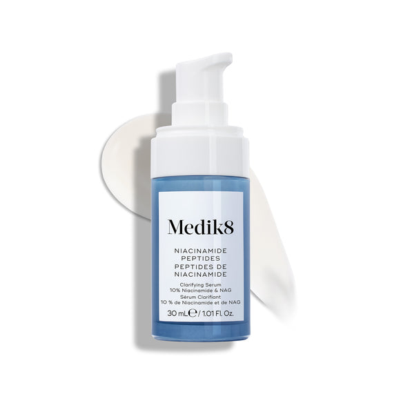 Botella de sérum Medik8 Niacinamide Peptides con un dispensador blanco, colocada sobre una superficie blanca con una pincelada de sérum blanco detrás.-15