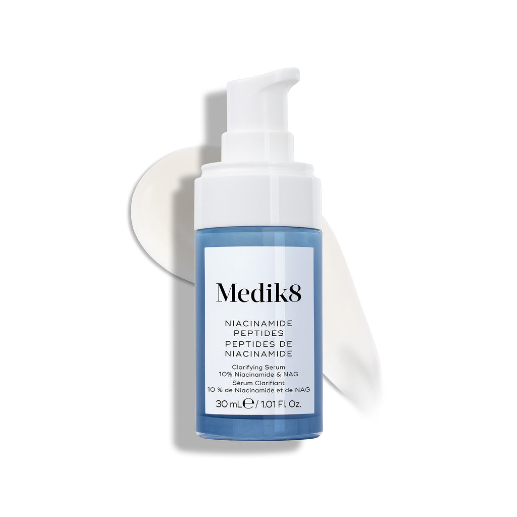 Botella de sérum Medik8 Niacinamide Peptides con un dispensador blanco, colocada sobre una superficie blanca con una pincelada de sérum blanco detrás.