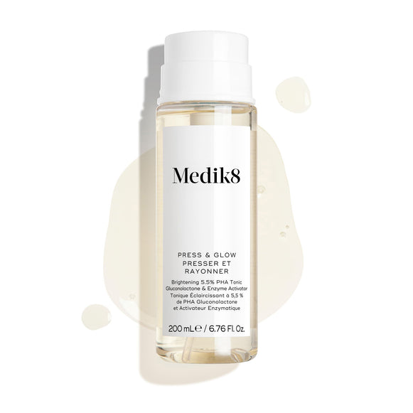 Botella del tónico Medik8 Press & Glow sobre un fondo blanco limpio con gotas translúcidas de líquido y un pequeño charco, destacando su textura acuosa. El texto identifica el producto como un tónico exfoliante diario con PHA y activador enzimático de 200 mL.