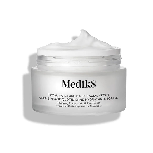 Tarro esmerilado de tamaño viaje de 12,5 ml de Medik8 Total Moisture Daily Facial Cream colocado junto a su caja de cartón blanca a juego. Los productos se muestran sobre una superficie gris texturizada, con un fondo blanco limpio. El texto en ambos indica: «Hidratación multicapa AM/PM con H.E.O.™ y péptidos prebióticos».-11