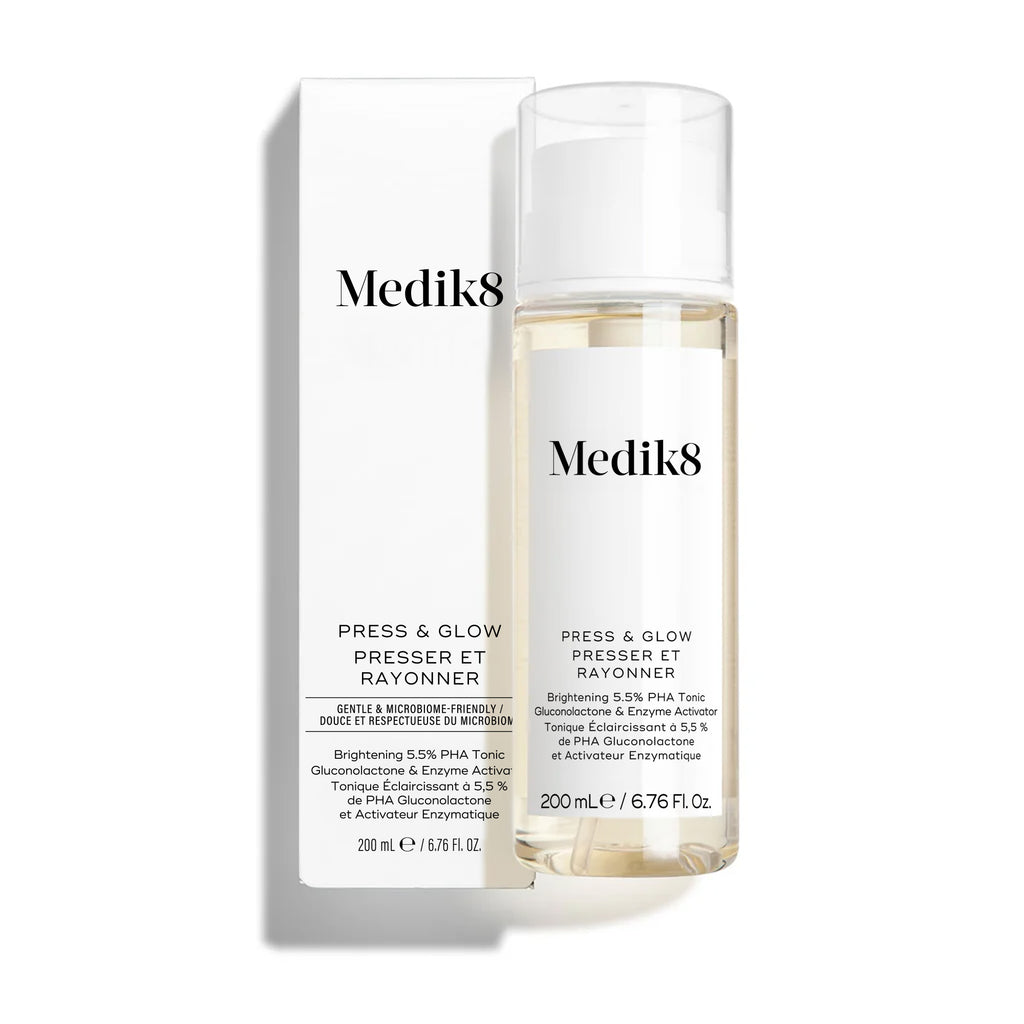 La botella del tónico Medik8 Press & Glow se encuentra frente a su caja blanca de producto a juego sobre un fondo blanco limpio. El texto en ambos identifica el producto como un tónico exfoliante diario con PHA y activador enzimático de 200 mL.