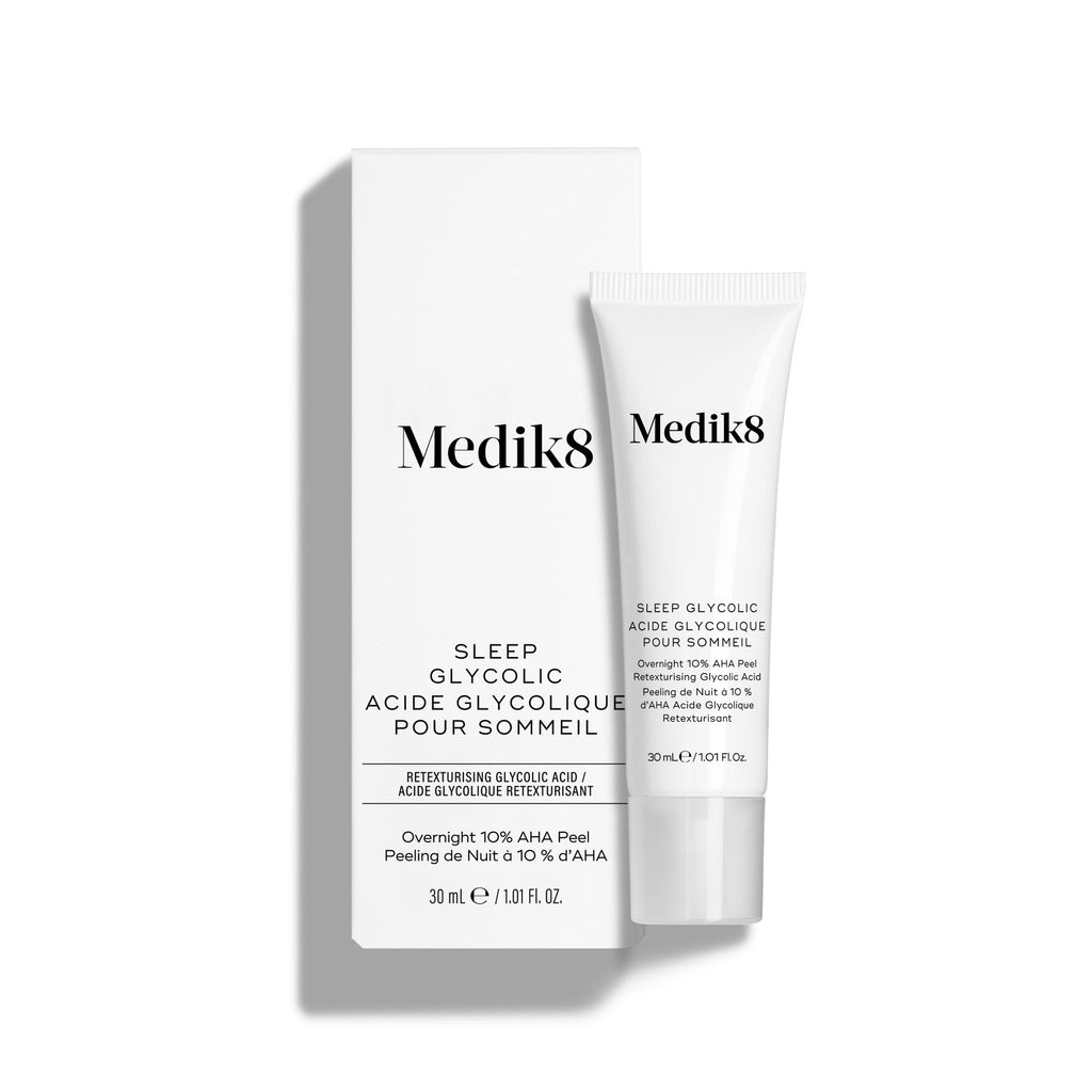 El tubo de Medik8 Sleep Glycolic aparece delante de su caja blanca a juego sobre un fondo blanco limpio. El texto tanto en el tubo como en la caja identifica el producto como un «Peeling nocturno con AHA de liberación prolongada para uso en casa» de 30 ml.
