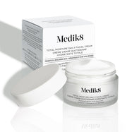 Tarro de vidrio esmerilado abierto de Medik8 Total Moisture Daily Facial Cream con una tapa blanca colocada a un lado, mostrando su rica crema blanca. El tarro se sitúa delante de su caja de cartón blanca sobre un fondo claro. El texto en ambos indica: «Hidratación multicapa AM/PM con H.E.O.® y péptidos prebióticos».
