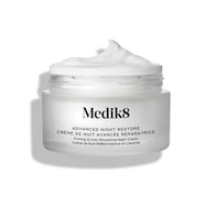 El tarro de crema Advanced Night Restore aparece abierto con una generosa porción de crema blanca en la parte superior, sobre un fondo blanco limpio, destacando su textura suave y reparadora. El texto negro del envase lo describe como “Crema de noche rejuvenecedora con multiceramidas”.