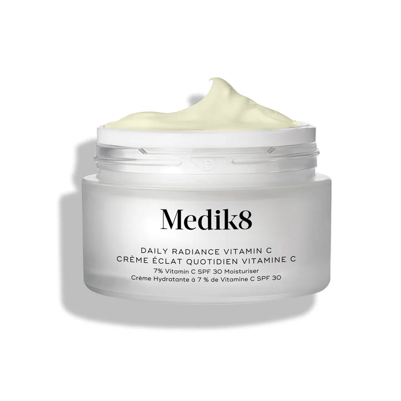 El tarro de cristal de Medik8 Daily Radiance Vitamin C aparece abierto con una generosa punta de crema amarillo pálido en la parte superior. El texto identifica el producto como una crema hidratante dos en uno C-Tetra Cream SPF 30 de 50 mL.