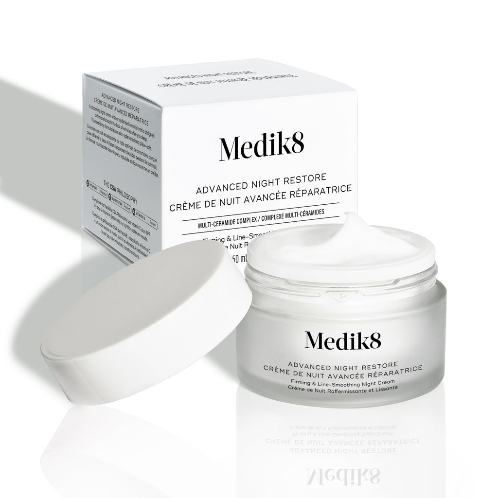 El tarro de crema Advanced Night Restore aparece abierto con su tapa blanca apoyada a un lado y la caja del producto detrás. La imagen muestra la textura rica de la crema y el diseño limpio del envase.