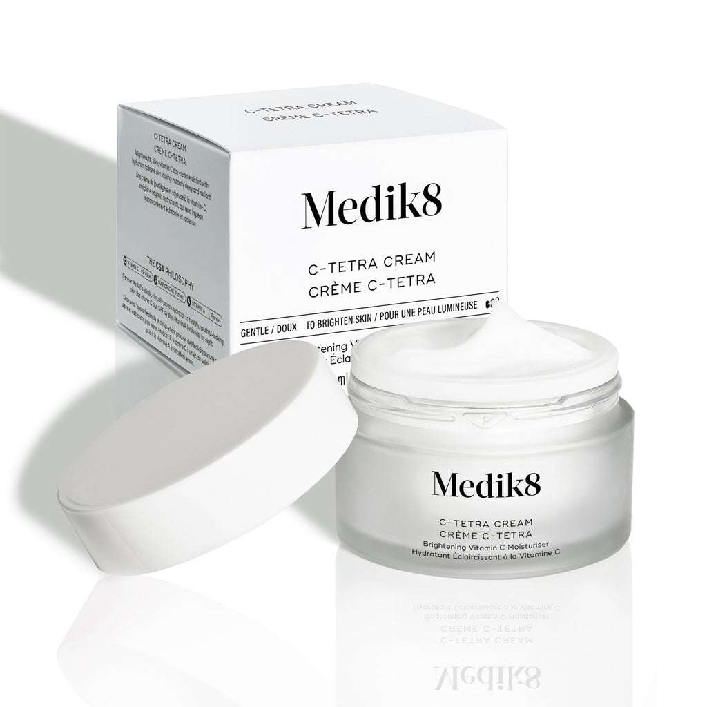El tarro de C-Tetra Cream y su caja de cartón blanca se muestran sobre un fondo blanco limpio con sombras suaves. El tarro de vidrio esmerilado abierto presenta el logotipo de Medik8 y la etiqueta “C-TETRA CREAM Lipid Vitamin C Radiance Cream” en formato de 50 mL. En la parte superior se ve una porción espesa de crema blanca, mientras la caja detrás muestra el nombre del producto y una lista parcial de ingredientes.