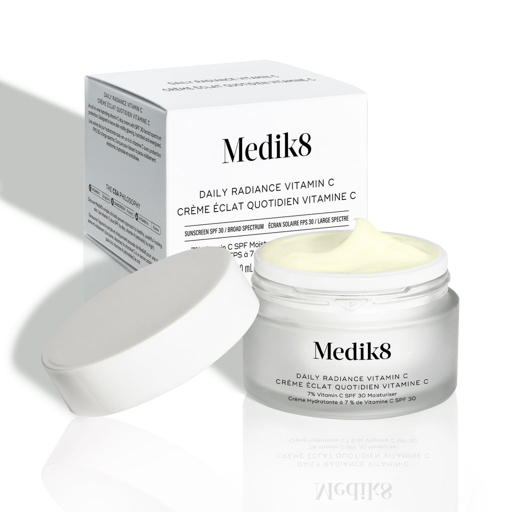La tapa abierta de Daily Radiance Vitamin C se muestra frente a la caja de cartón del producto, con la textura de la crema visible.