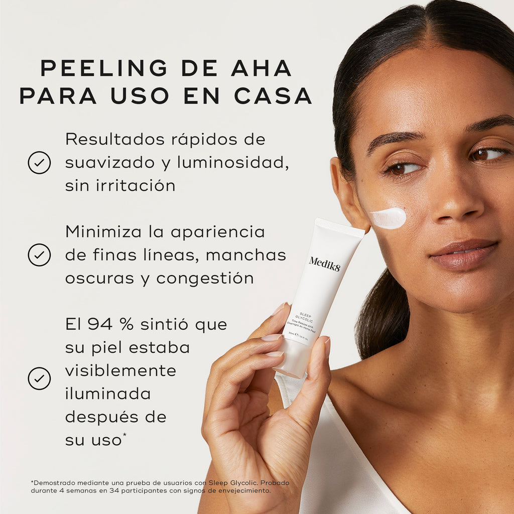 Una persona sostiene un tubo de Medik8 Sleep Glycolic sobre un fondo neutro color blanco roto con una muestra de crema blanca aplicada en la mejilla. El texto destaca sus beneficios como un «Peeling AHA para uso en casa» que «proporciona resultados rápidos de suavidad y luminosidad sin irritación» y «minimiza la apariencia de líneas finas, manchas oscuras y congestión». También señala: «El 94 % sintió que su piel estaba visiblemente más luminosa tras su uso».
