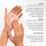 Primer plano de unas manos creando una espuma ligera, destacando los ingredientes clave de Medik8 Surface Radiance Cleanse. El texto describe los AHA (ácido mandélico y ácido láctico) para la exfoliación superficial, los BHA (ácido salicílico) para descomponer la congestión de los poros y la glicerina para hidratar y humectar la piel.