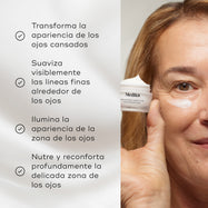 Una mujer rubia sostiene un tarro abierto esmerilado de Medik8 Advanced Night Eye cerca de su rostro, que tiene una pequeña aplicación de crema blanca debajo del ojo. La etiqueta lo identifica como una “Crema Rejuvenecedora para el Contorno de Ojos”, sobre un fondo blanco limpio.