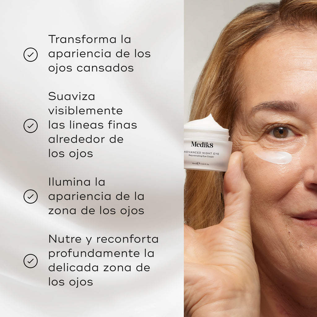 Una mujer rubia sostiene un tarro abierto esmerilado de Medik8 Advanced Night Eye cerca de su rostro, que tiene una pequeña aplicación de crema blanca debajo del ojo. La etiqueta lo identifica como una “Crema Rejuvenecedora para el Contorno de Ojos”, sobre un fondo blanco limpio.