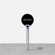 Un exprimidor metálico plateado de tubos de Medik8 en posición vertical sobre una superficie gris. El cabezal circular presenta el logotipo de Medik8, diseñado para ayudar a dispensar el producto de forma eficiente.
